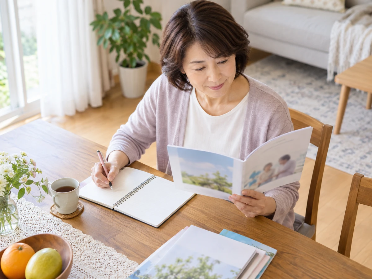 自宅で冊子を読みながらノートにメモを取る女性。