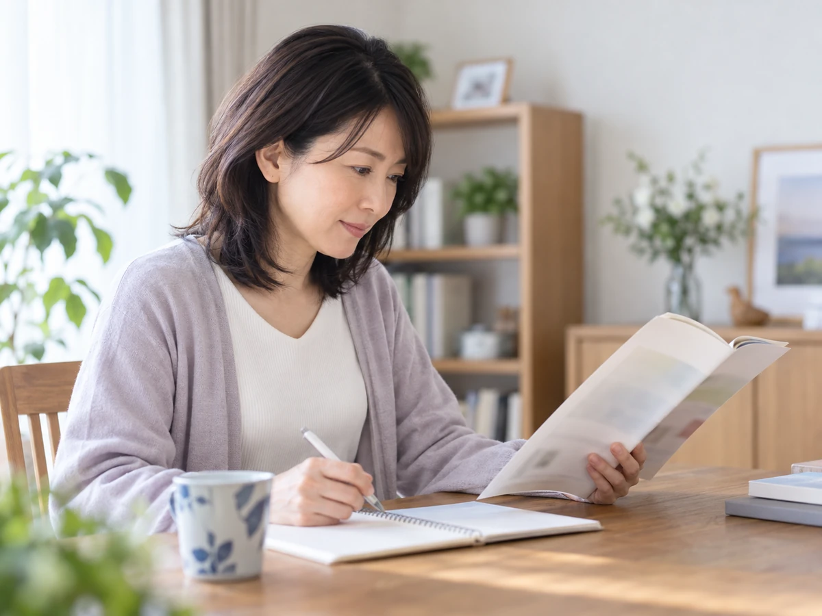 冊子を読みながらノートに情報を整理する女性。