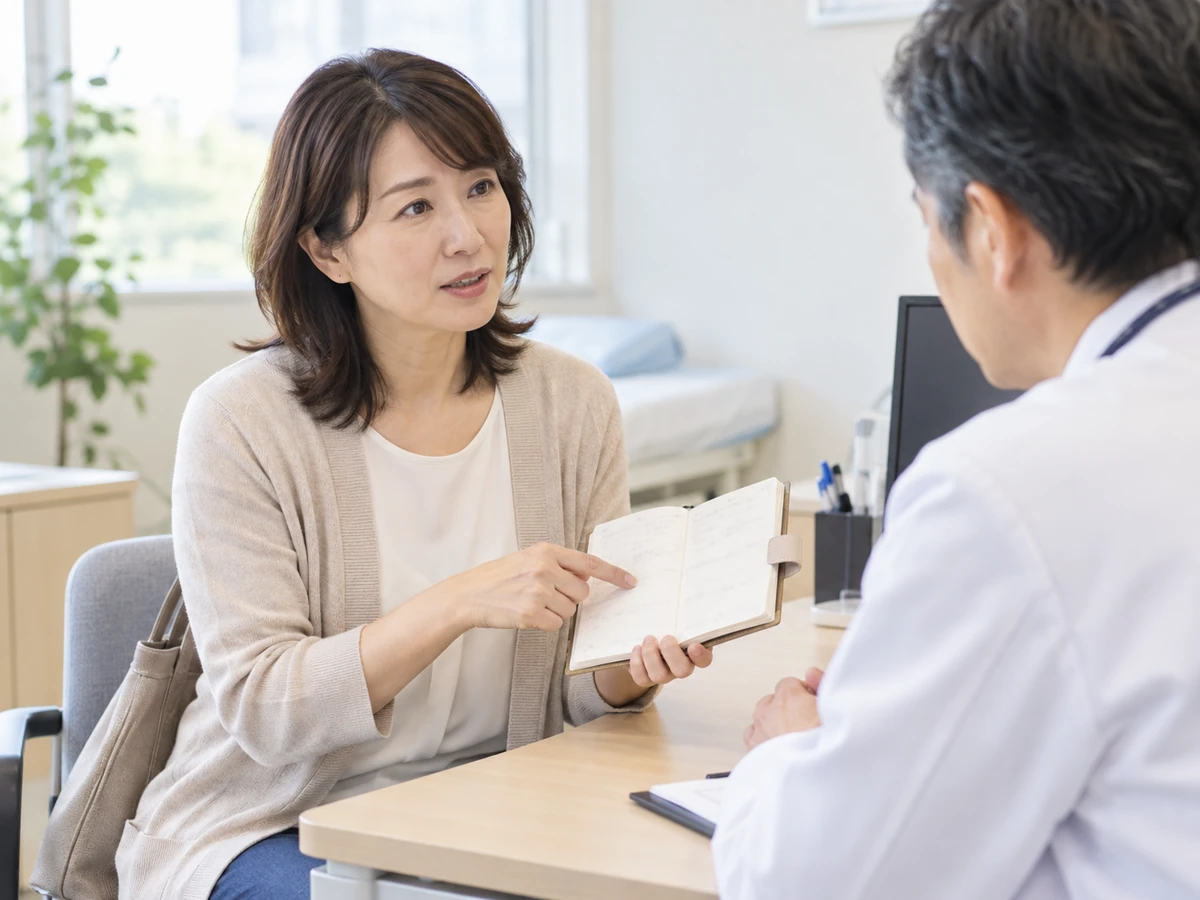 診察室で女性が手帳を示しながら医師に体調を伝えるイメージ。