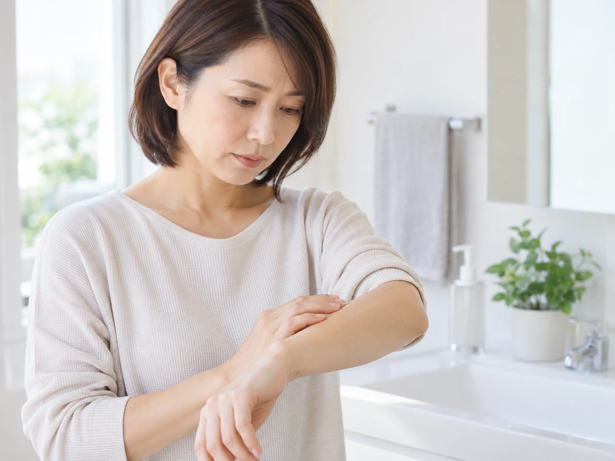 自宅の洗面室で、女性が前腕の皮膚を確認している。