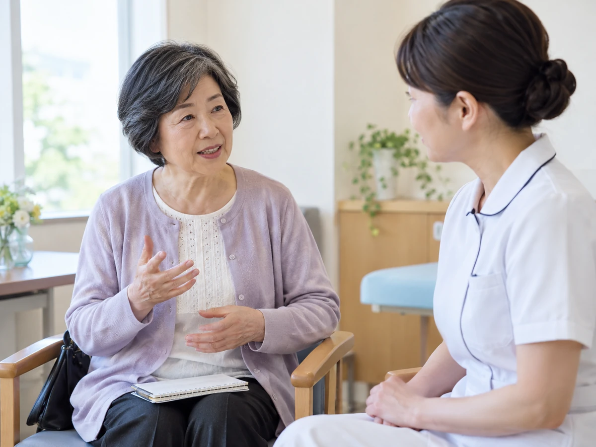 ひざにノートを置いた女性が、看護師に体調について話している。