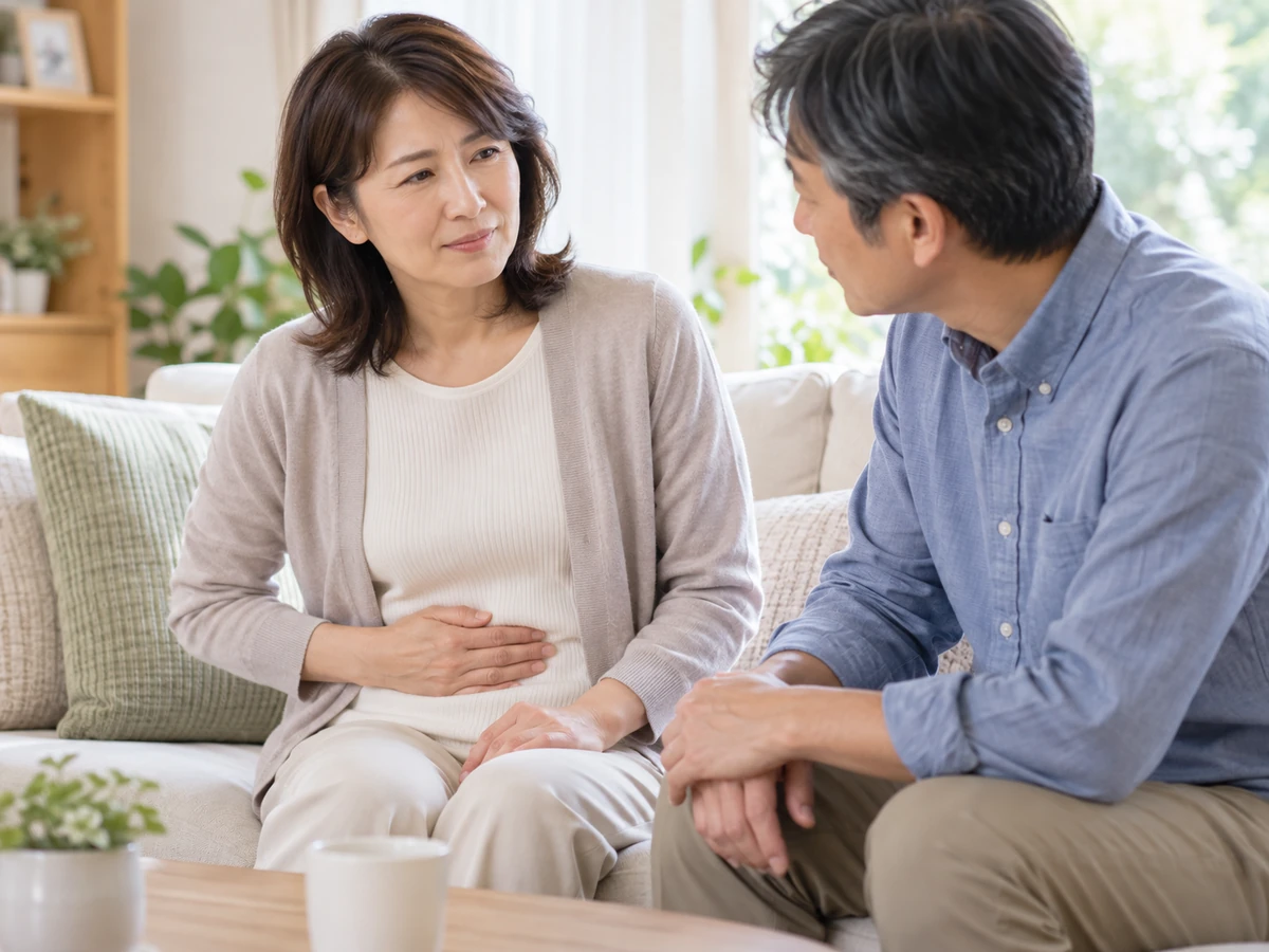 おなかに手を添えた女性の話を、自宅のソファで家族が聞く様子