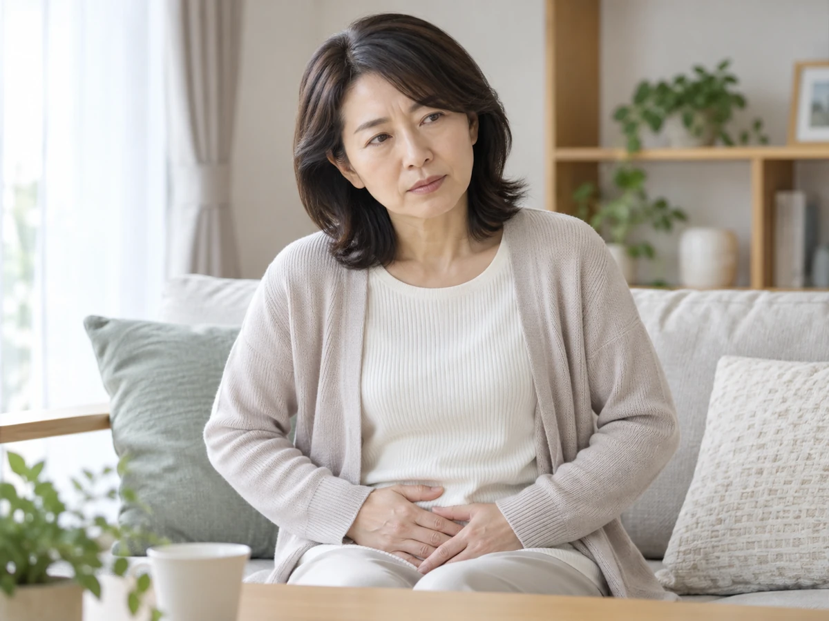 自宅のソファに座り、おなかに手を当てて体の変化を気にする女性。