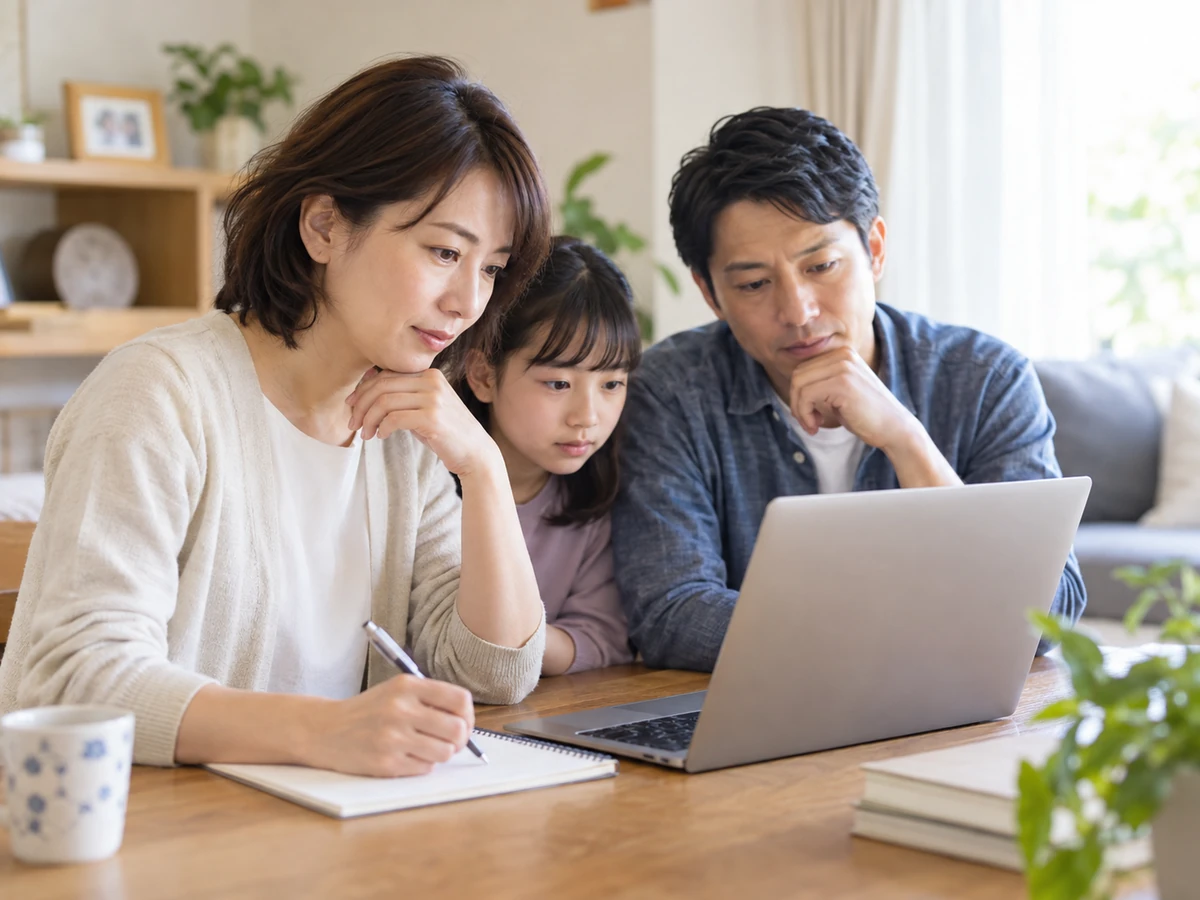 家族が自宅でノートパソコンを一緒に見て、女性がノートに記録している。