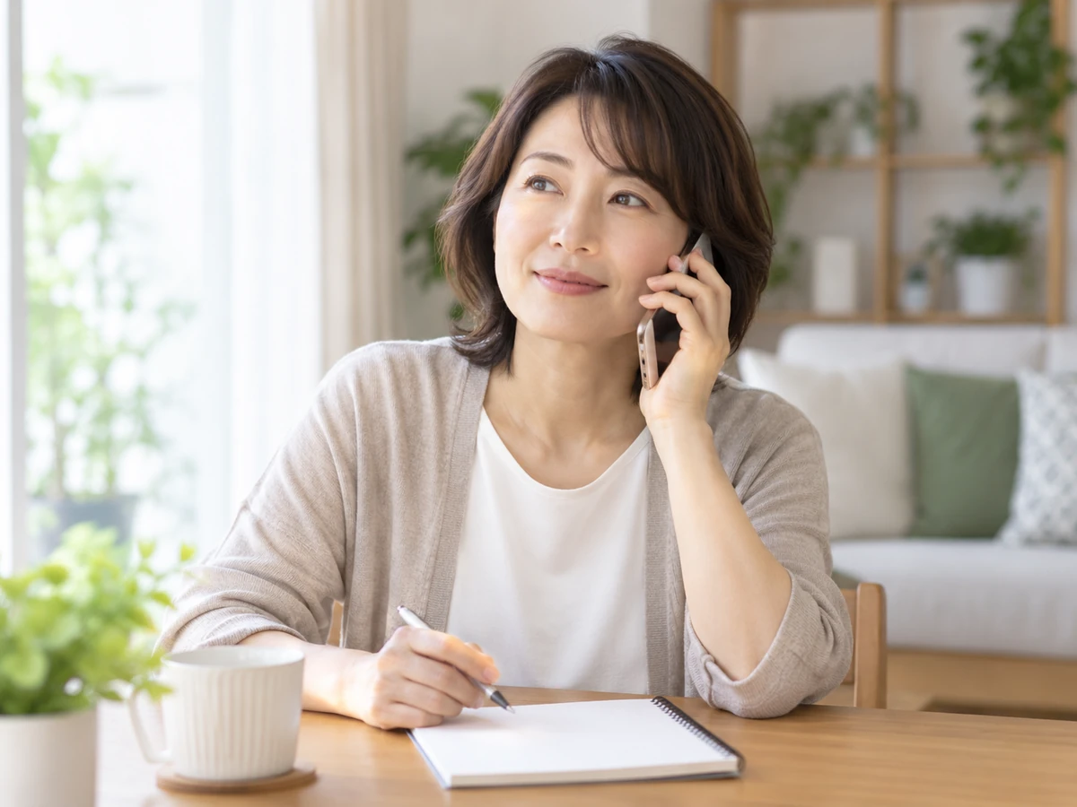 自宅でノートとペンを用意して電話で相談する女性の写真
