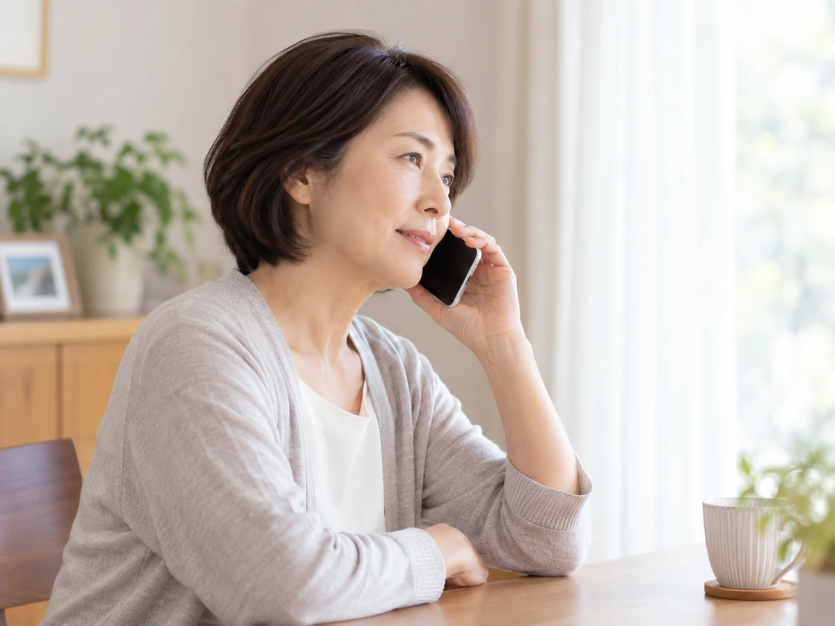 自宅で女性がスマートフォンを耳に当てて相談している。